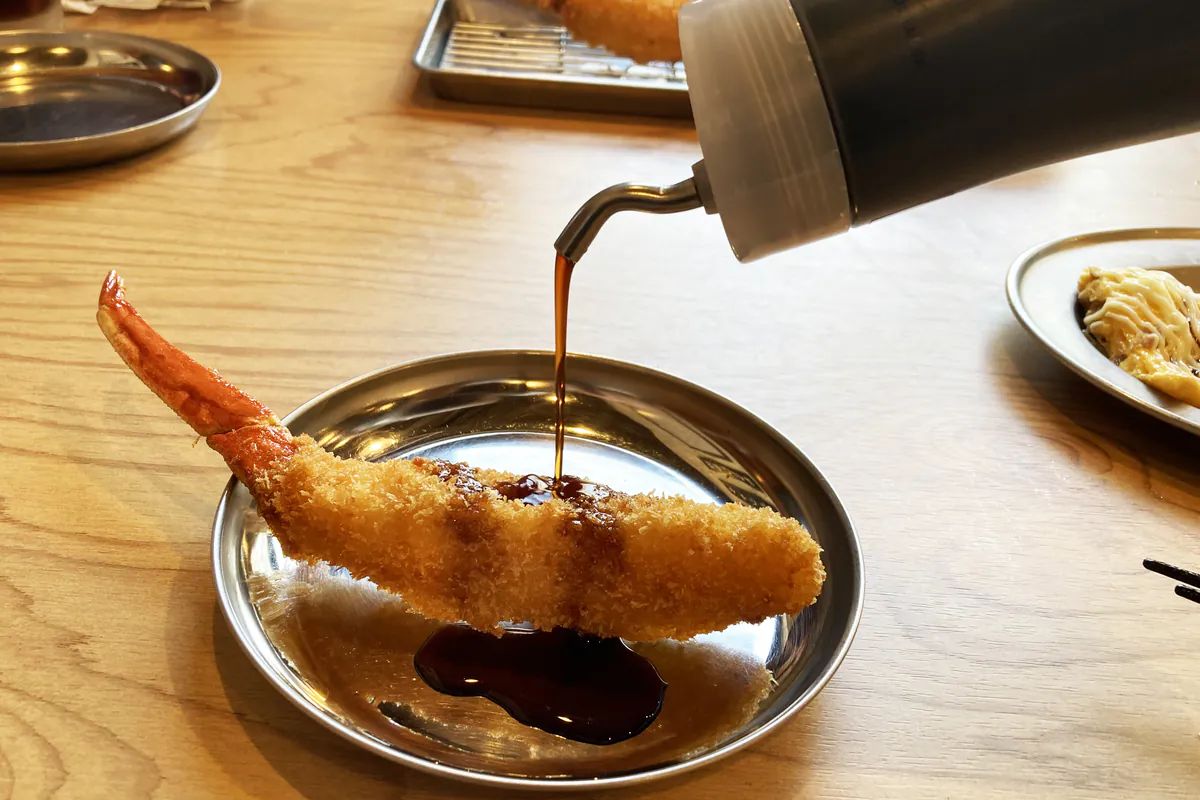 秘伝の自家製ソースをかけているえびの串カツ